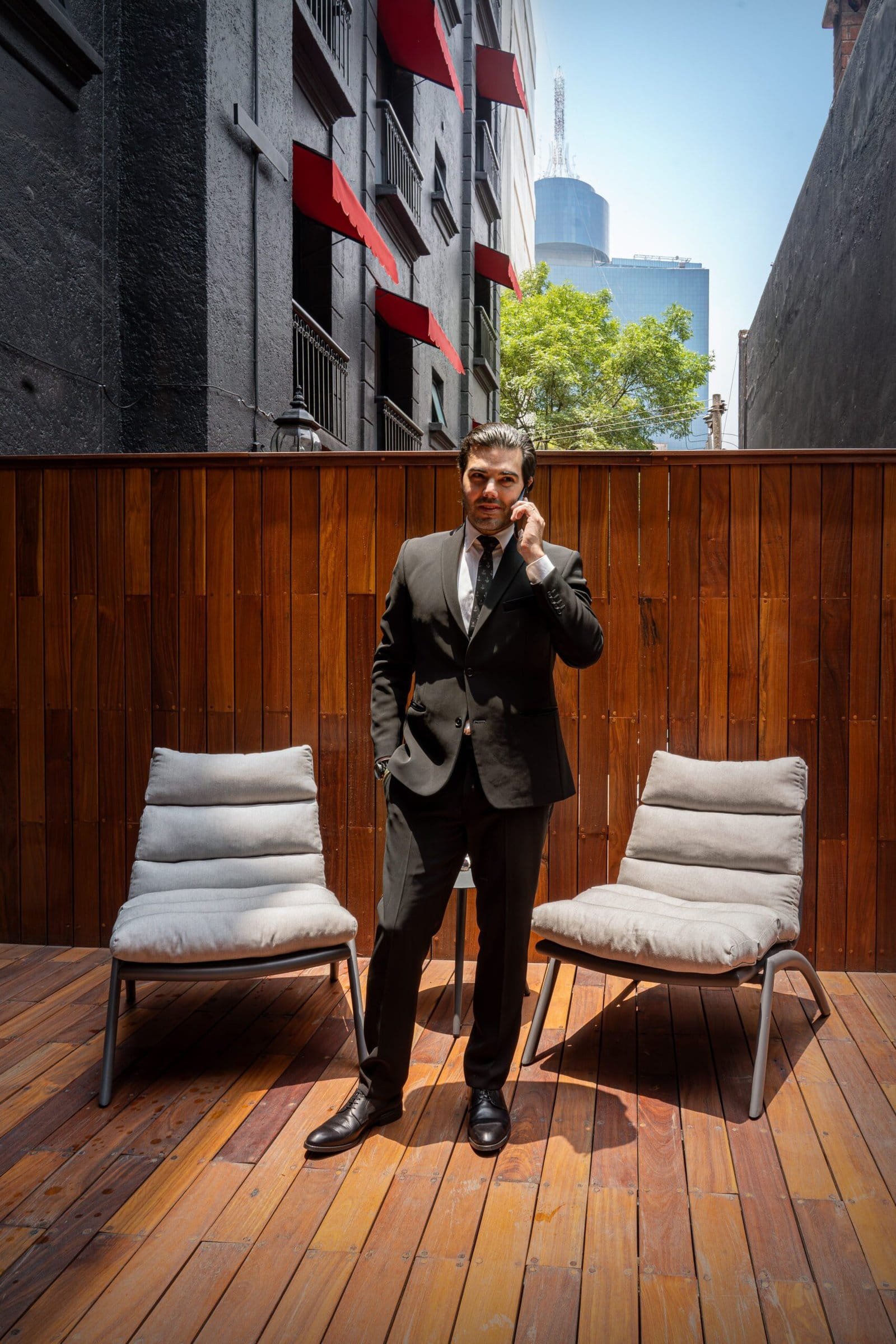 Modelo masculino elegantemente vestido, en la terraza de una habitación del hotel en la Ciudad de México, hablando por teléfono.