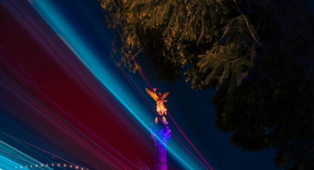 Ángel de la Independencia iluminado de noche con destellos de luces azules y moradas."